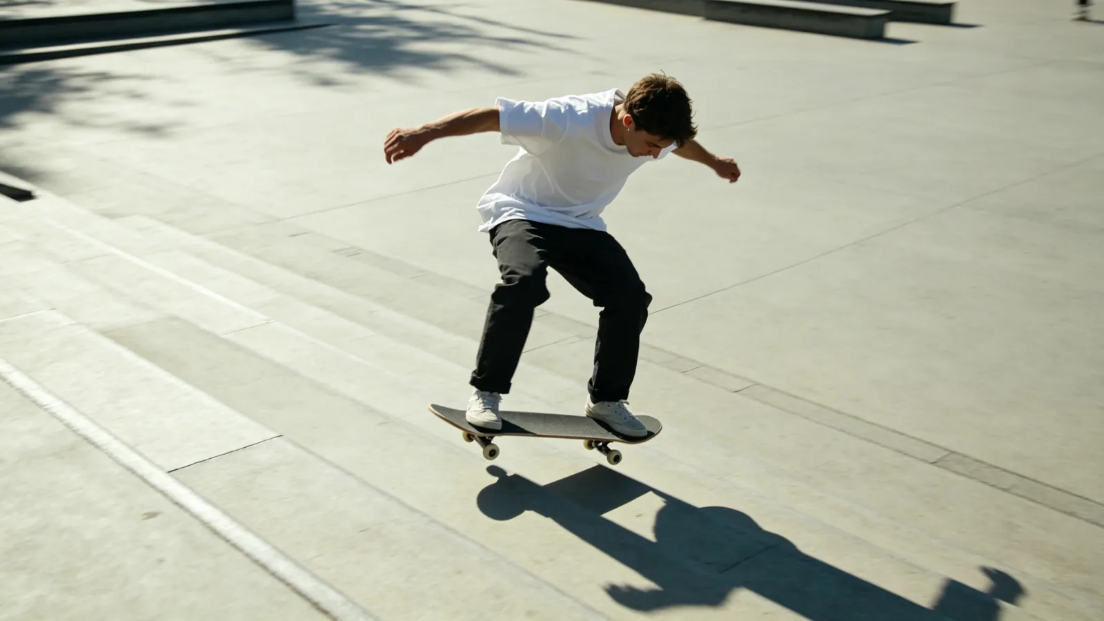 Un skater flota en pleno ollie sobre unas escaleras en una plaza vacía y soleada.